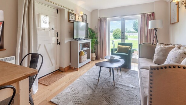 A cozy living room with a television, a sofa, a dining table, and a view of the outdoors through large windows. - 1 bedroom accommodation in Bognor Regis (Bognor Regis)