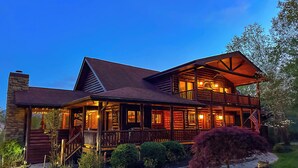 Une cabane en rondins à deux étages, dotée d’un balcon, de fondations en pierre et d’un jardin bien entretenu.
