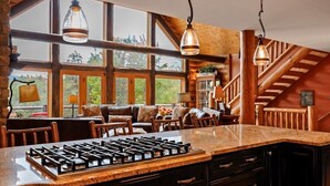Une cuisine dotée d’un grand îlot central, de meubles en bois et offrant une vue sur l’extérieur grâce à de grandes fenêtres.