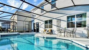A swimming pool with a sunshade structure, outdoor seating, and a view of a house in the background. - BV310MB - Disney & Universal heroes - 16 guests (Kissimmee)