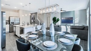 A modern kitchen with a central island, stainless steel appliances, and a dining area with a glass table set for four. - BV310MB - Disney & Universal heroes - 16 guests (Kissimmee)