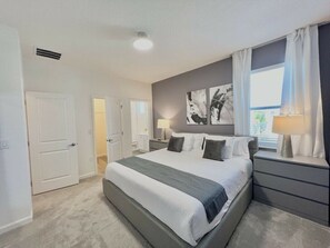 Ein Schlafzimmer mit einem großen Bett, Nachttischen, einem Fenster mit Vorhängen und einem an der Wand hängenden Kunstwerk.