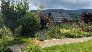 A house with a sloped roof surrounded by lush greenery and a paved pathway. - Gemütliche Ferienwohnung Über 2 Etagen mit Garten und Kamin, Haustierfreundlich! (Oberwiesenthal)