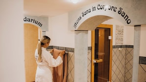 A person in a white robe hanging a towel in a bathroom with tiled walls and a wooden door. - Gemütliche Ferienwohnung Über 2 Etagen mit Garten und Kamin, Haustierfreundlich! (Oberwiesenthal)