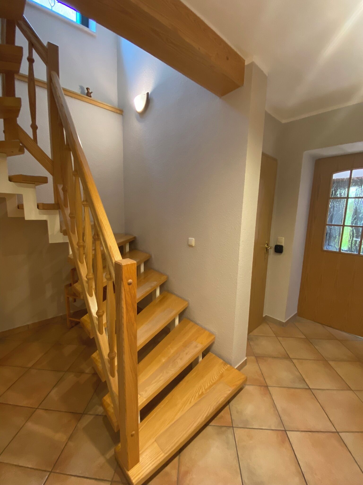 A wooden staircase with a handrail, a light fixture on the wall, and a door with a window.