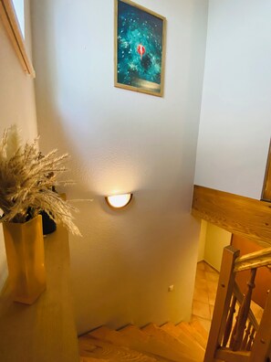Una escalera con barandilla de madera, una lámpara de pared y un cuadro enmarcado.