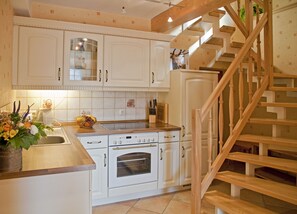Una cocina con armarios blancos, una escalera de madera y un lavamanos con un cuenco de frutas.