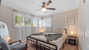 A bedroom with a bed, a chair, a bedside table with a lamp, a ceiling fan, and a window with blinds. - Ladoga's Hideway, Gorgeous Pool, Game Room, Fire Pit, Private Backyard,BBQ Grill (Long Beach)
