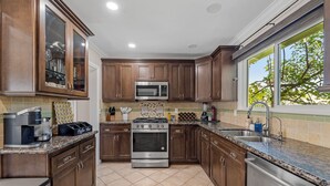 A kitchen with wooden cabinets, stainless steel appliances, a tiled backsplash, and a window with a view of trees. - Ladoga's Hideway, Gorgeous Pool, Game Room, Fire Pit, Private Backyard,BBQ Grill (Long Beach)