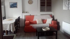 A cozy living room with a red sofa, a small table, and a dining area with chairs.