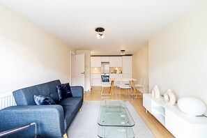 Un salon moderne avec un canapé, une table basse en verre et un coin repas comprenant une table et des chaises blanches.