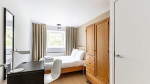 A bedroom with a bed, a desk, a chair, a wardrobe, and a window with curtains.