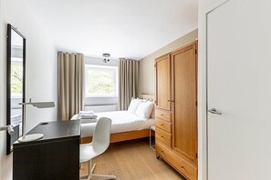 A bedroom with a bed, a desk, a chair, a wardrobe, and a window with curtains.