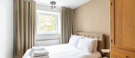 Een hotelkamer met een bed, nachtkastje, kledingkast en raam met gordijnen.