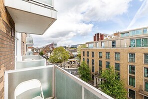 Ein modernes Gebäude mit Glasfassade, einem Innenhof mit Sitzgelegenheiten und Blick auf die Stadtlandschaft.