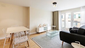 A modern living room with a glass coffee table, a sofa, a dining table with chairs, and a white cabinet.
