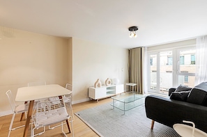 A modern living room with a glass coffee table, a sofa, a dining table with chairs, and a white cabinet.