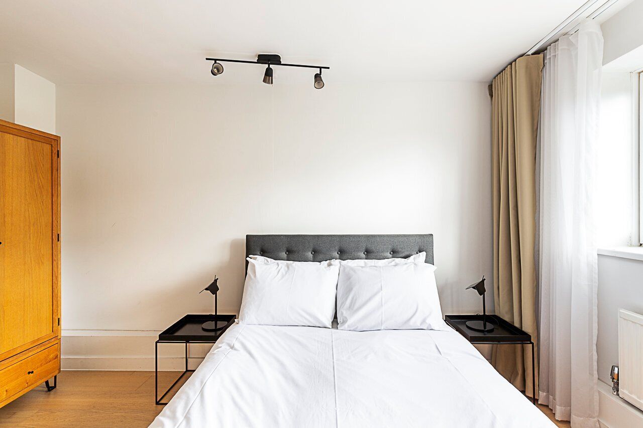 A bedroom with a bed, two bedside tables, a wardrobe, and a ceiling light fixture.