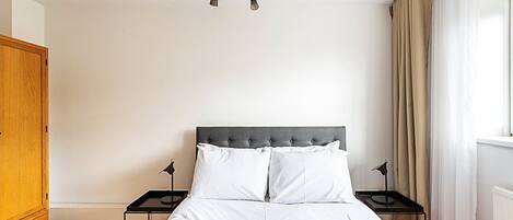 A bedroom with a bed, two bedside tables, a wardrobe, and a ceiling light fixture.