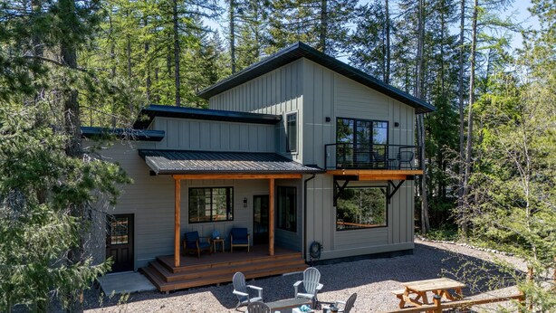 A modern two-story cabin with a deck, outdoor seating, and a view of the surrounding forest. - Glacier Natl Park & River Views, Dog Friendly (Hungry Horse)