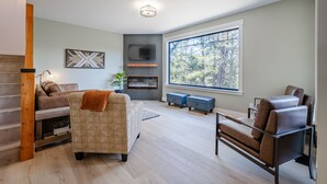 A modern living room with a fireplace, a large window, and a staircase. - Glacier Natl Park & River Views, Dog Friendly (Hungry Horse)