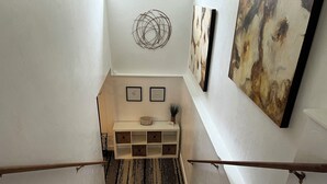 Un escalier avec des marches en bois, un mur blanc et une petite table ornée d’objets décoratifs.