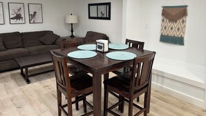 Un coin repas avec une table et des chaises en bois, un canapé, une lampe et des œuvres d’art encadrées accrochées au mur.