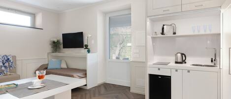 A compact kitchen with a dishwasher, a coffee maker, and a window with blinds.
