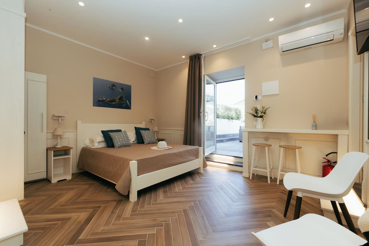 Ein modernes Hotelzimmer mit einem großen Bett, einem Schreibtisch, zwei Stühlen und Blick ins Freie.