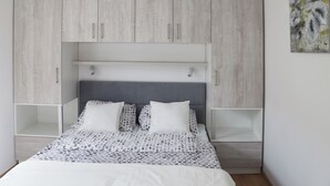 Un dormitorio con cama, ropa de cama blanca y gris a lunares, cabecero gris y armarios de madera clara.