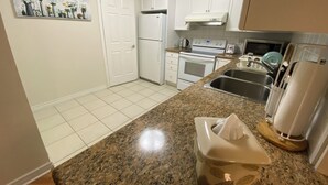A kitchen with white cabinets, a granite countertop, a refrigerator, an oven, a microwave, a sink, and a painting on the wall.