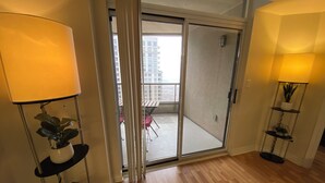 A modern apartment with a sliding glass door leading to a balcony, wooden flooring, and two floor lamps.