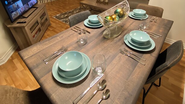 A dining area with a wooden table set for four, light blue plates, and silverware. A television is on a stand to the left.