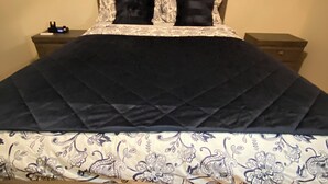 A bed with a dark quilt and floral-patterned bedspread, flanked by two nightstands with drawers, and three framed abstract artworks on the wall above.