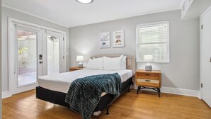 Een slaapkamer met een bed, nachtkastjes, een raam met zonwering en een deur met ruit.
