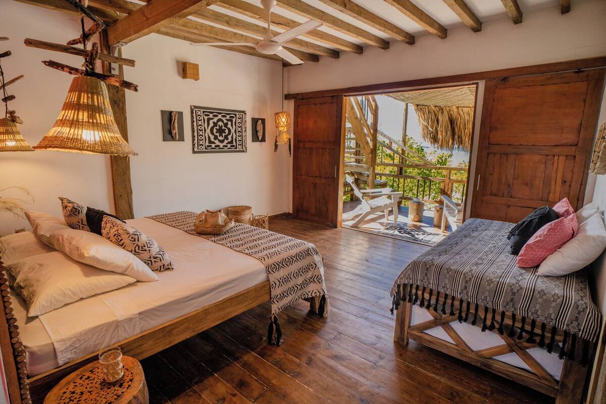 A spacious bedroom with two beds, wooden flooring, and a large sliding door leading to an outdoor area.