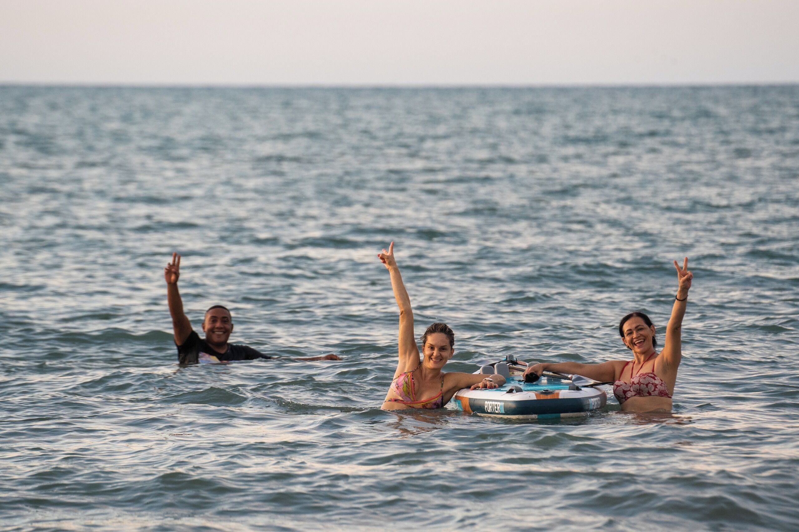 Three people floating on a body of water, one of them on a floating device.