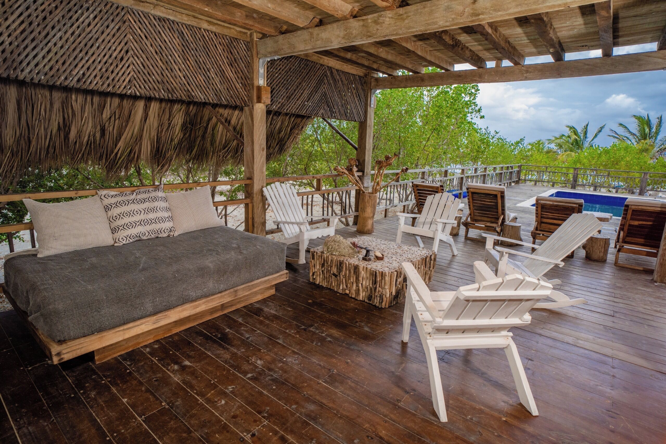 A covered outdoor seating area with a wooden deck, a sofa, and several Adirondack chairs.