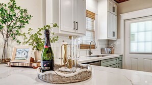 Una cocina con armarios blancos, encimera de mármol, una botella de vino espumoso y un cuadro enmarcado.