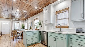 Una cocina con alacenas verde claro, lavavajillas y techo de madera.