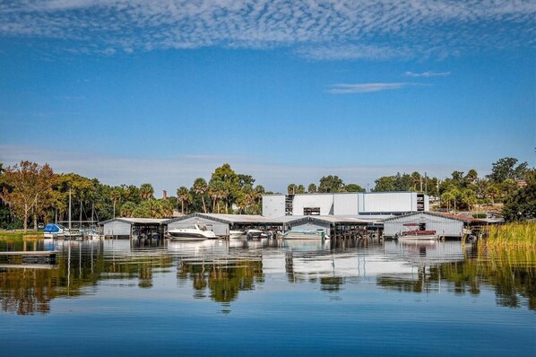 A marina with boats docked, a large industrial building, and a calm water body reflecting the surroundings.