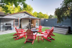 A backyard with a covered patio area, a grill, and red Adirondack chairs.