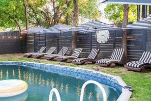 A backyard with a swimming pool, lounge chairs, and a clock on a wall.