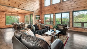 A spacious living room with a large black leather sofa, a wooden coffee table, and a dining area with a table and chairs. - Smoky Horizon by Avantstay Game Room, Movie Theater, Deck w Hot Tub Views! (Sevierville)