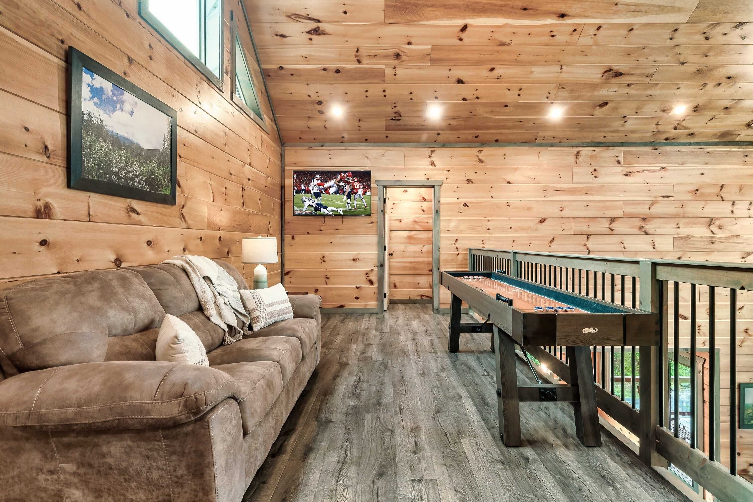A cozy room with wooden walls, a sofa, a pool table, and a TV screen displaying a sports game.