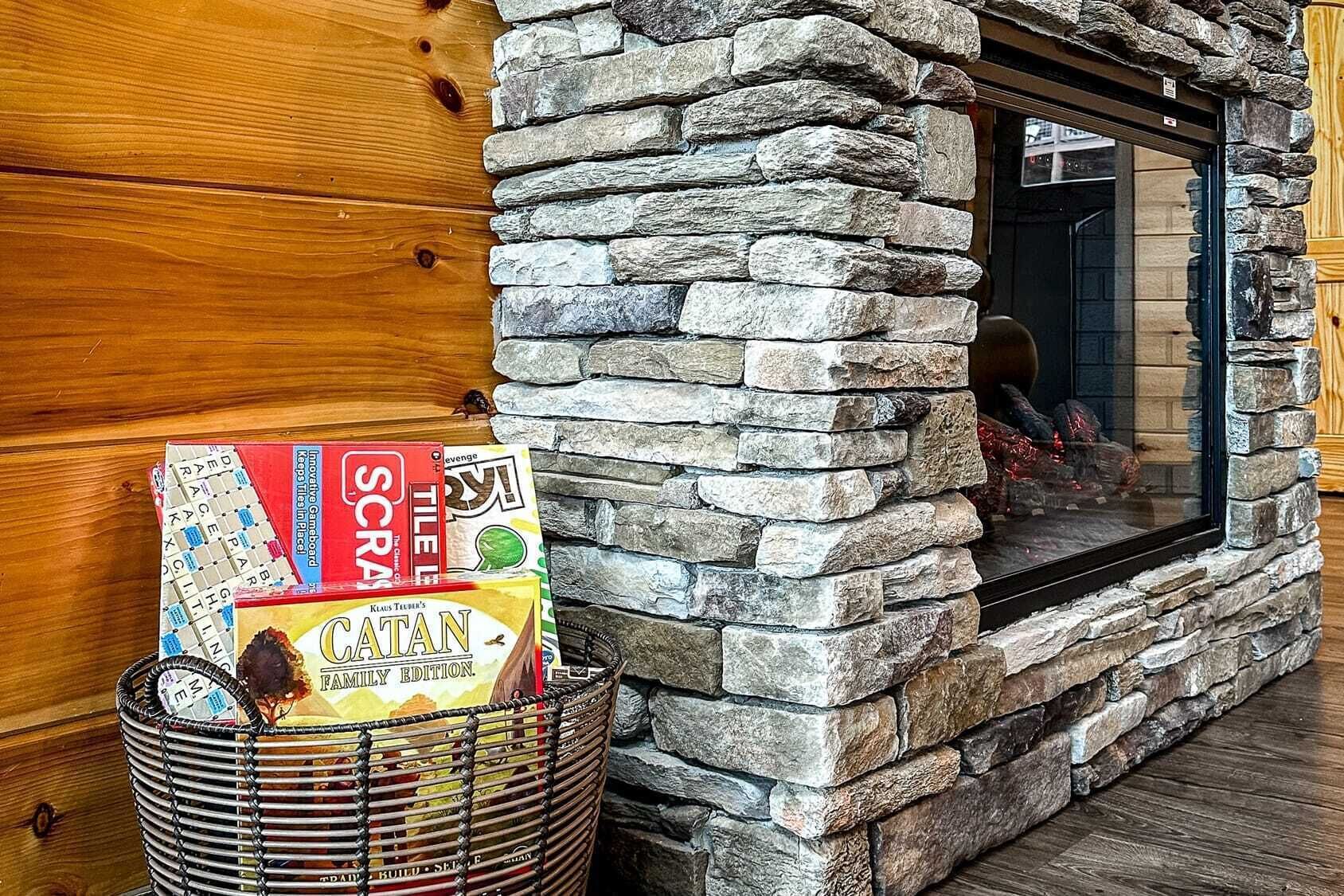 A stone fireplace with a window, a wooden wall, and a basket with board games.