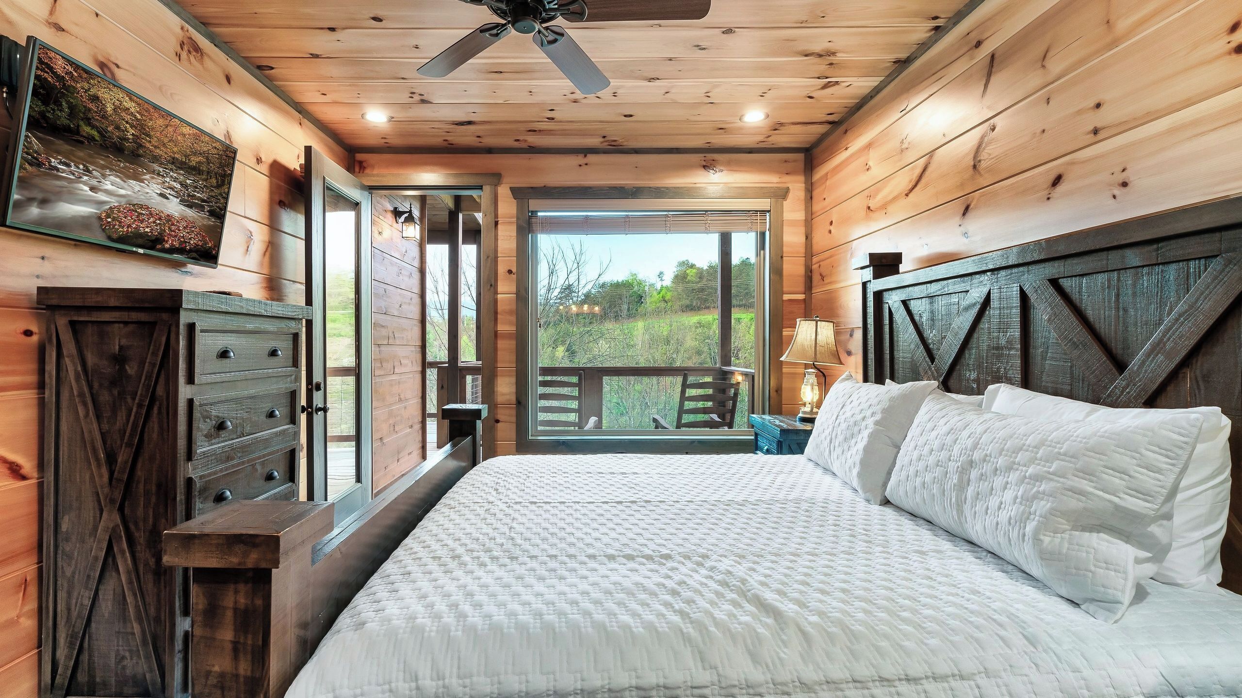 A wooden cabin bedroom with a bed, dresser, and a view of the outdoors.