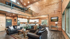 A spacious living area with a high ceiling, wooden walls, a dining area, and a kitchen. - Smoky Horizon by Avantstay Game Room, Movie Theater, Deck w Hot Tub Views! (Sevierville)