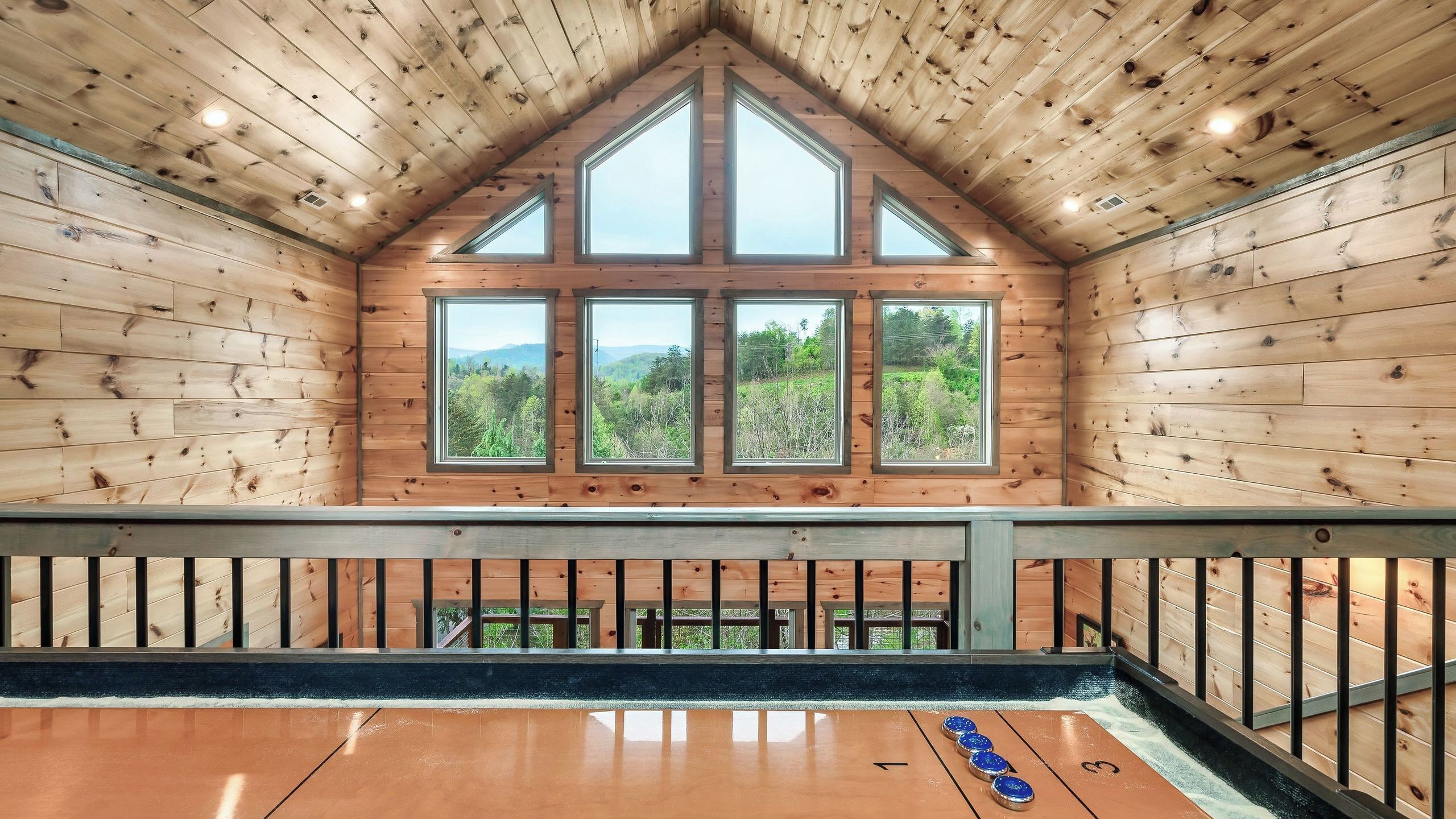 A wooden cabin with a loft bedroom featuring a large window with a view of a forested landscape.