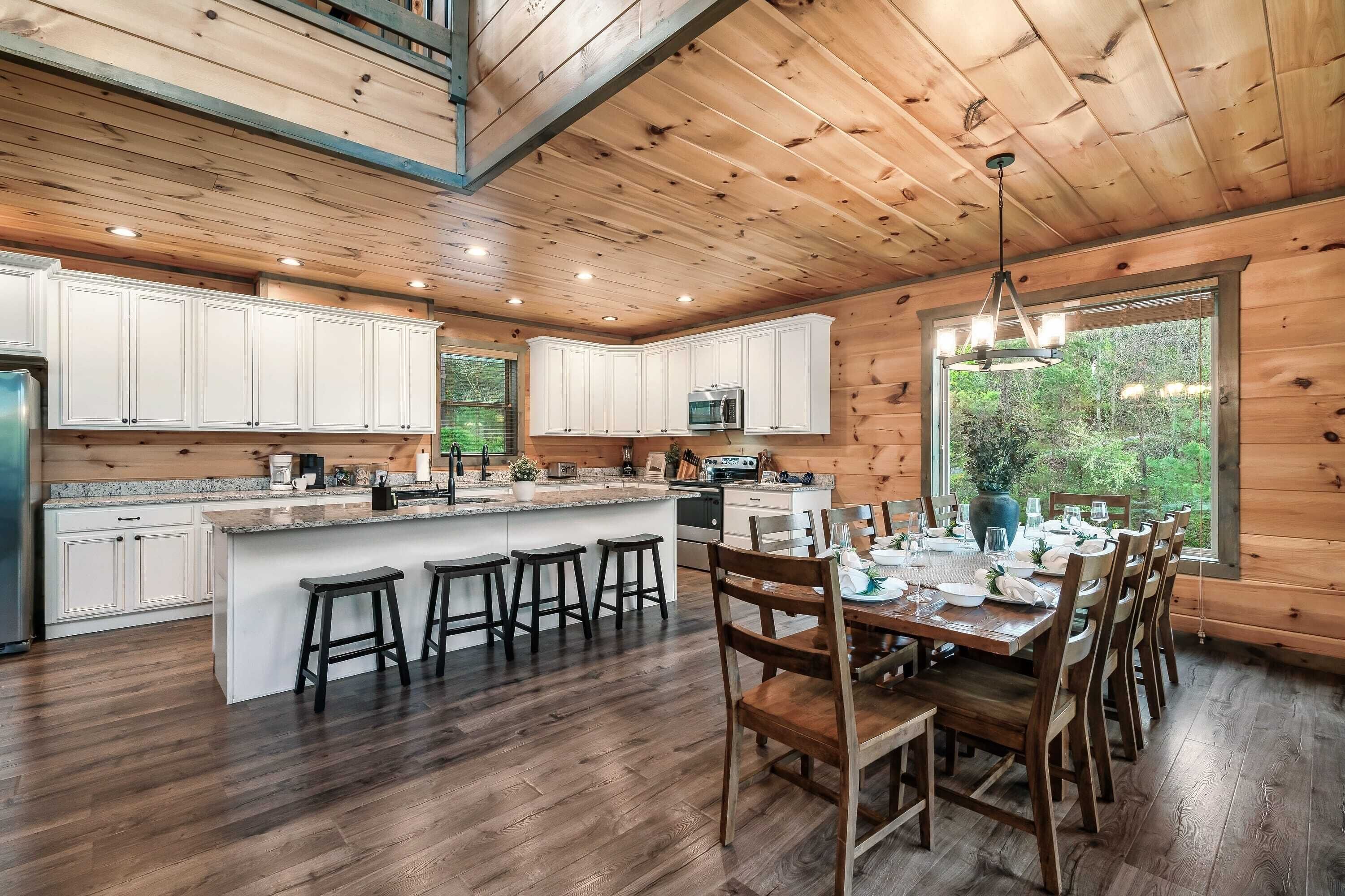 Una cocina amplia con armarios de madera, una isla central con taburetes y un comedor con un gran ventanal.